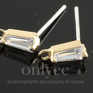 May include: Two gold-tone earring findings with a clear rectangular crystal. Each finding has a loop at the top and a post at the bottom.