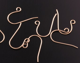 May include: Five gold-toned earring hooks, made of metal, are arranged on a black surface. The hooks are designed with a loop at the top and a curved wire that extends down to a point.