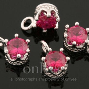 Pode incluir: Quatro pingentes de prata em forma de coroa com pedras de cristal rosa. Cada pingente tem um laço para prender a um colar ou pulseira.