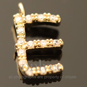 Puede incluir: Encanto de letra E dorada con diamantes de imitación transparentes. El encanto es una opción popular para la elaboración de joyas y manualidades.