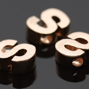 May include: Three rose gold letter beads in the shape of the letter "S".