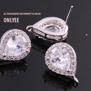 May include: A pair of silver teardrop earrings with clear cubic zirconia stones. The earrings have a halo setting and a post back.
