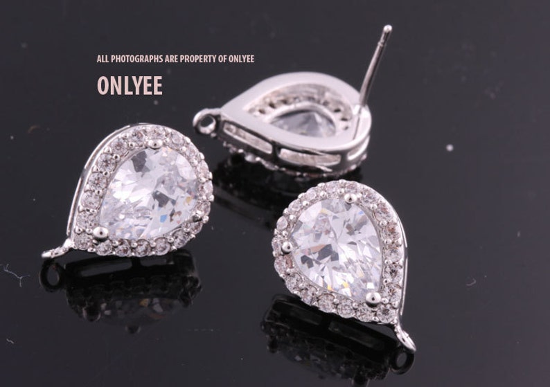 May include: A pair of silver teardrop earrings with clear cubic zirconia stones. The earrings have a halo setting and a post back.
