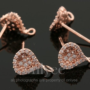 May include: Two rose gold earring findings with a teardrop shape and a clear crystal design. The findings have a loop on the side for attaching a dangle charm.