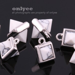 May include: A group of six silver and white pyramid and square shaped charms with a loop for hanging. The charms are made of metal and have a white stone in the center.