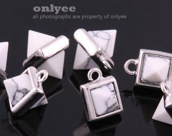 May include: A group of six silver and white pyramid and square shaped charms with a loop for hanging. The charms are made of metal and have a white stone in the center.