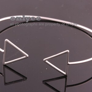 May include: A silver bangle bracelet with two triangle shapes on the ends. The bracelet is open and can be adjusted to fit different wrist sizes.