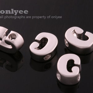 May include: Four silver letter C beads with a hole through the center. The beads are designed to be used for jewelry making.