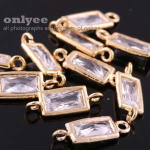 Op de afbeelding: Gouden metalen connector charms met heldere rechthoekige kristalaccenten. De charms hebben aan elk uiteinde een lus om aan sieraden te bevestigen.
