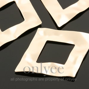 May include: Four gold-colored metal squares with a square hole in the center. Each square has a small hole on one side.