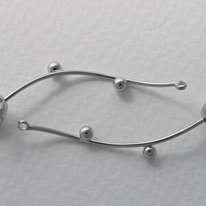 May include: Two silver-toned, curved metal earring components. Each component features a floral design at one end and a small loop at the other. Small, round beads are spaced along the curved stems. These components are suitable for jewelry making.