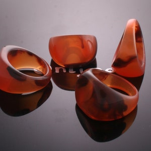 May include: Four brown and black marbled resin rings. The rings are all different shapes and sizes.