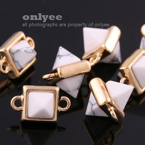 May include: Close-up of gold-colored jewelry findings with white and black marbled stone accents. The findings have a geometric design with square and triangular shapes. The text "onlyee" and "all photographs are property of onlyee" is visible.