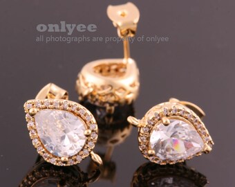 May include: Gold-toned teardrop earrings with a large, clear, pear-shaped stone at the center, surrounded by smaller, clear stones. The earrings have a decorative, ornate design.