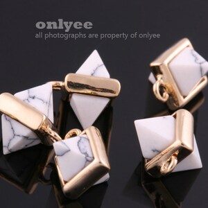 May include: Three gold and white geometric pendant charms. The charms are in the shape of a pyramid, a square, and a rhombus. The charms are made of white marble with gold accents.