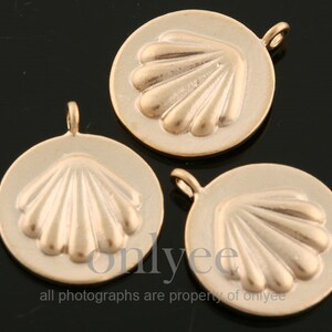 May include: Three gold-colored round pendants with a seashell design. Each pendant has a small loop at the top for attaching to a chain or other jewelry component. The seashell design is raised and detailed.