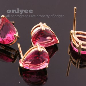 May include: A pair of gold earrings with pink teardrop-shaped stones. The earrings have a simple design and are perfect for everyday wear.