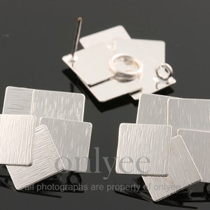 May include: Silver-toned geometric earrings with a textured, brushed finish. Each earring features multiple square and rectangular shapes arranged in a cluster. The earrings are displayed on a dark surface.