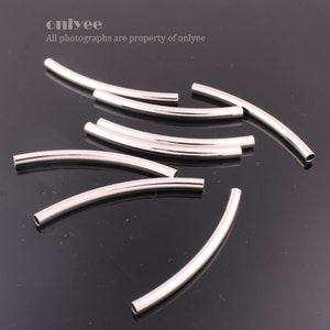 May include: A group of ten silver-toned metal curved tube beads. The beads are arranged in a random pattern on a black surface.