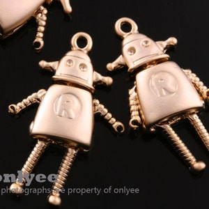 May include: Gold-toned robot charm with a letter R on the chest. The charm has a loop at the top for attaching to a necklace or bracelet.