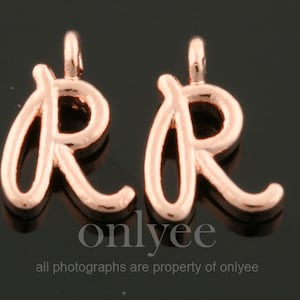 May include: Two rose gold letter R charms. The charms are in a cursive font style.