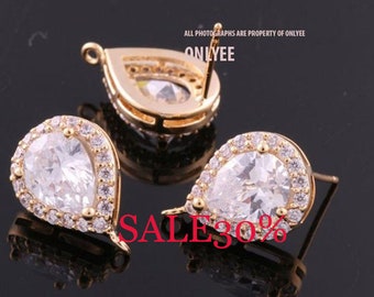 May include: A pair of gold teardrop earrings with clear cubic zirconia stones. The earrings have a halo setting and a post back.