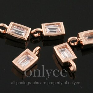 Op de afbeelding: Vier roségouden metalen bedels met heldere rechthoekige kristallen. Elke bedel heeft een lus om aan een ketting of armband te bevestigen.