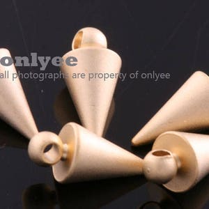 May include: Five gold-coloured metal cone-shaped charms with a loop at the top. The charms are arranged in a cluster on a black surface.