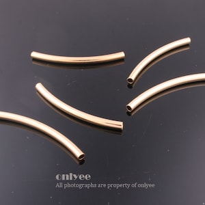 May include: Five gold-colored metal bead spacers, each with a slight curve. The spacers are arranged in a semi-circle pattern on a black surface.