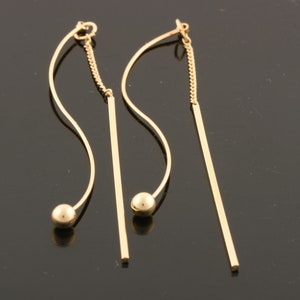 May include: A pair of gold dangle earrings with a long, straight bar and a curved bar with a small gold ball at the end.