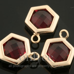 May include: Three gold-toned hexagonal charms with a red crystal in the center. Each charm has a loop on the top for attaching to jewelry.