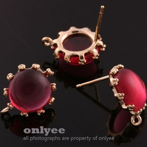 May include: Three gold-tone earring findings with red glass cabochons. Each finding has a post and a loop.
