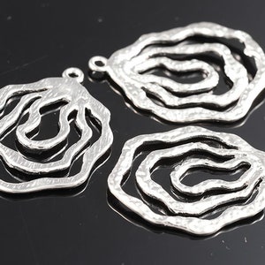 May include: Two silver metal pendant charms with a layered, wavy, circular design. The charms have a textured, hammered finish.
