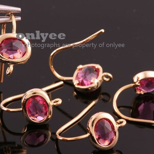 May include: Five gold earring hooks with pink oval-shaped gemstones. The hooks are made of metal and have a shiny finish.