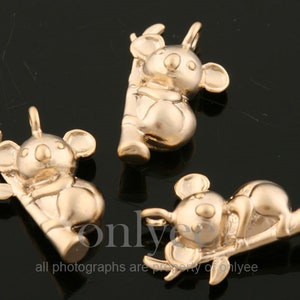May include: Three gold-colored koala bear charms, each sitting on a branch. The charms are detailed and have a realistic appearance.