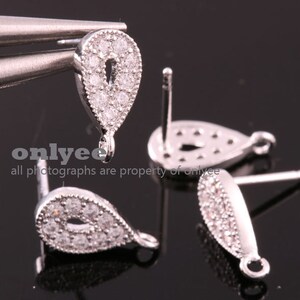 May include: Three silver teardrop-shaped earring findings with clear crystal accents. Each finding has a post and a loop for attaching a charm or bead.