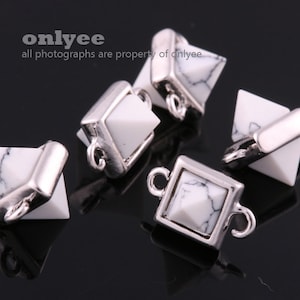 May include: Five silver and white pyramid-shaped charms with a loop on each side. The charms are made of metal and have a white stone in the center.