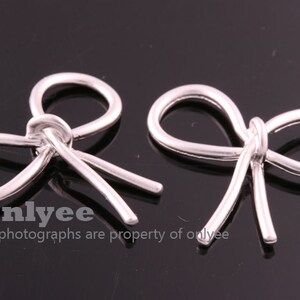 May include: Two silver metal bow-shaped charms. The charms are made of a single piece of wire that is bent into a bow shape.