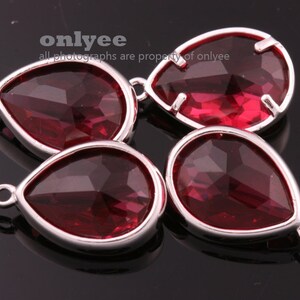 May include: Four teardrop-shaped crystal pendants with silver-toned metal settings. The crystals are a deep red color.
