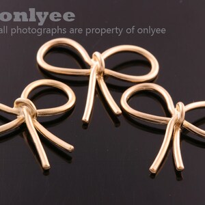 May include: Three gold-coloured metal bow shapes. The bows are all the same size and shape, but they are arranged in a staggered pattern. The bows are on a black background.
