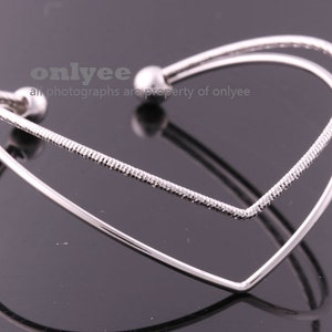 May include: A silver double-layered heart-shaped bangle bracelet. The bracelet has a textured finish on the top layer and a smooth finish on the bottom layer.