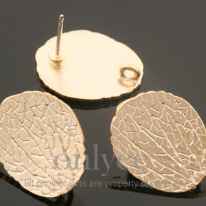 May include: A pair of gold-tone leaf-shaped earrings with a textured surface. The earrings have a post back closure.