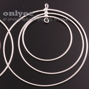 May include: Silver hoop earrings with a twisted rope design. The earrings are layered in three sizes, with the largest hoop on the outside.