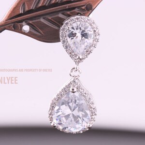 May include: A pair of silver teardrop earrings with clear cubic zirconia stones. The earrings have a halo setting and a dangling pear-shaped stone.