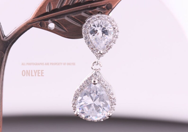 May include: A pair of silver teardrop earrings with clear cubic zirconia stones. The earrings have a halo setting and a dangling pear-shaped stone.