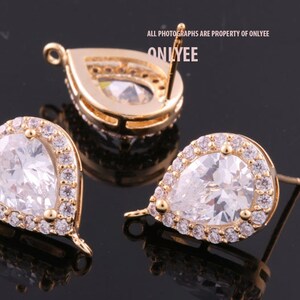 May include: A pair of gold-tone teardrop-shaped earrings with clear cubic zirconia stones. The earrings have a halo setting and a post back.