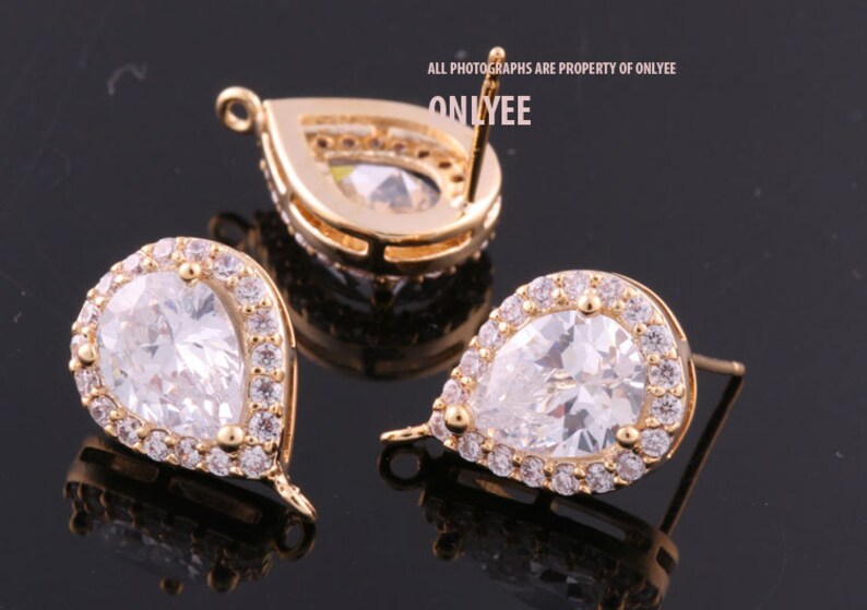 May include: A pair of gold-tone teardrop-shaped earrings with clear cubic zirconia stones. The earrings have a halo setting and a post back.