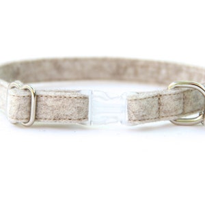 May include: A beige felt cat collar with a silver buckle, a clear plastic safety release buckle, and a silver bell.