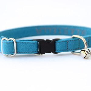 May include: A turquoise blue felt cat collar with a black plastic buckle and a silver bell. The collar has a silver D-ring for attaching a lead.