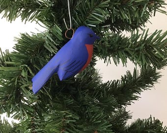 Peut inclure: Ornement d'oiseau bleu avec une poitrine rouge suspendu à un sapin de Noël. L'oiseau est en bois et possède un crochet en fil de fer. L'arbre a des aiguilles vertes.